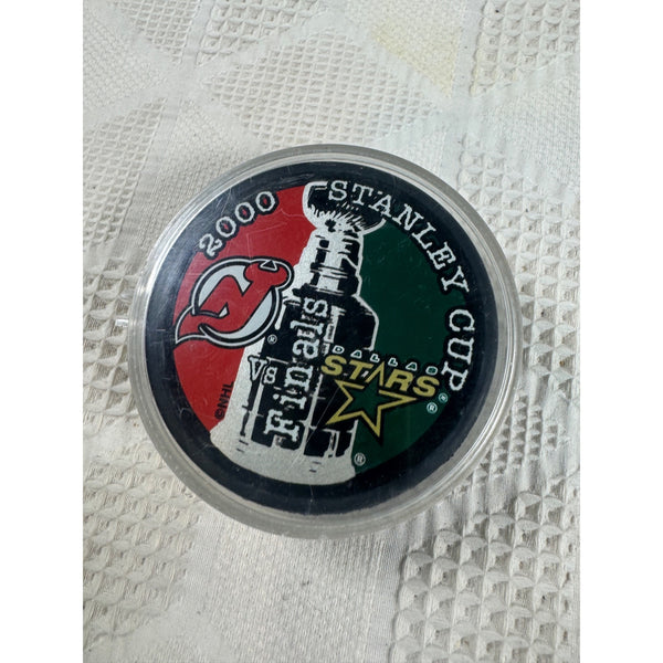 2000 Stanley Cup Finals Hockey Puck New Jersey Devils Vs Dallas Stars NHL. A 2000 Stanley Cup final puck inside a clear plastic protective case, featuring the New Jersey Devils team logo and the word 'Stars' on a textured white fabric background.