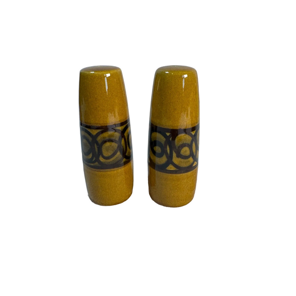 Vintage Brixham Pottery Ceramic Salt & Pepper Shakers Yellow Brown Pattern 1970s. A pair of vintage ceramic salt and pepper shakers with a glossy mustard yellow glaze and a dark brown band featuring a repeating circular pattern, set on a white textured surface against a light gray wall.