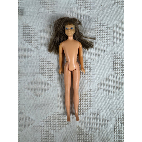 Vintage 1960s Skipper Doll Little Sister Of Barbie Brunette Hair Blue Eyes Japan. A vintage bare-faced doll with long brown hair and blue eyes, lying on a textured white quilted blanket.