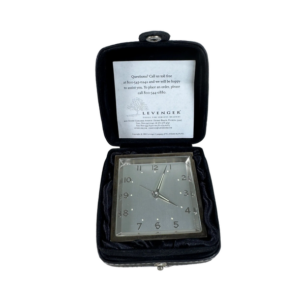 Levenger Silver Desk Clock In Black Travel Case With Fold Out Stand. An open Levenger pocket watch case with a black velvet interior, showing a silver-toned square watch face with a glass cover and a white insert card with text inside the lid.