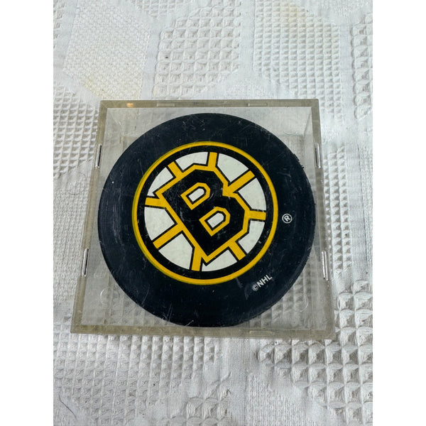Boston Bruins Official Licensed NHL Hockey Puck in Display Case InGlasCo . A black hockey puck featuring the Boston Bruins logo, displayed inside a clear acrylic block on a textured white surface.