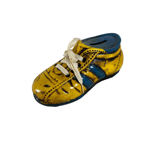 Vintage Enesco Ceramic Shoe Bank Yellow and Blue Hand Painted 1970s Retro. A small yellow and blue toy shoe with cream-colored laces, resting on a textured white fabric background.