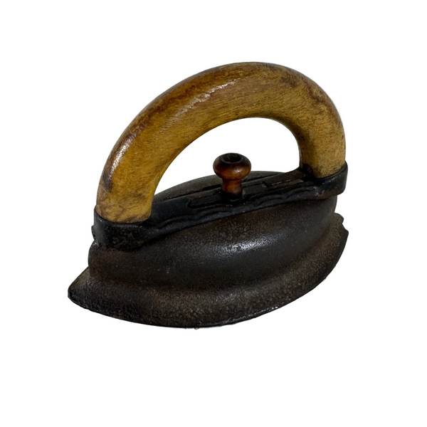 Antique Cast Iron Sad Iron With Wooden Handle Primitive Home Decor 1904. An antique cast iron iron with a curved wooden handle and a dark metal sole, resting on a textured white fabric surface.
