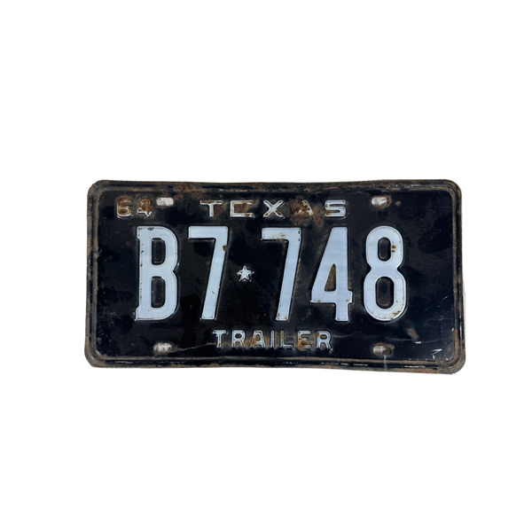 Vintage 1964 Texas Trailer License Plate Black w White Embossed Background B7748. A vintage Texas license plate for trailers, featuring the black background with white lettering and the number sequence B7 748, displayed on a textured white surface.