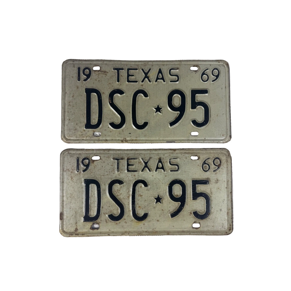 Vintage 1969 Texas License Plates Pair DSC 95 White w Embossed Black Lettering. Two vintage 1969 Texas license plates with the registration 'DSC 95' printed in black on an off-white background, displayed on a textured white surface. 