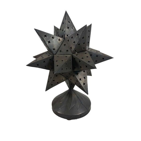 Punched Tin Star Shaped Tea Light Holder With Decorative Base Rustic Metal . A dark gray, multi-pointed star-shaped metal lantern or decorative sculpture with star-shaped cutouts, displayed on a textured white surface against a light gray background.