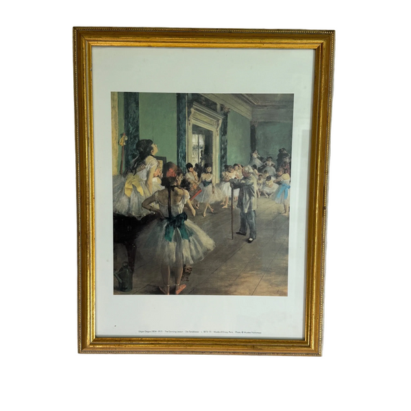 Edgar Degas The Dancing Lesson Framed Wall Art Print In Gold Frame Vintage. A framed art print depicting a classical ballet rehearsal scene, featuring ballerinas in white tutus and a male dancer in a gray suit, enclosed in a gold frame and mounted on a textured white wall.