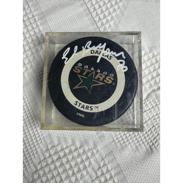 Dallas Stars NHL Official Game Puck Signed By Ed Belfour With Display Case. An autographed Dallas Stars hockey puck inside a clear acrylic display case, resting on a textured white fabric background.