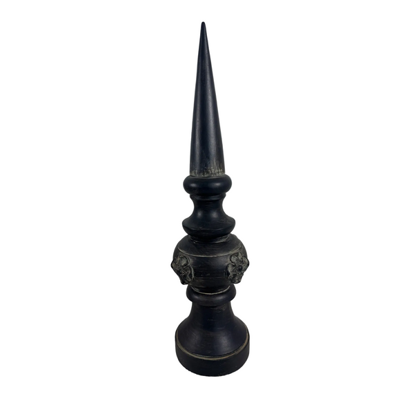 Decorative Resin Architectural Finial w Embossed Scroll Design Tabletop Shelf . A dark, ornate decorative finial or candlestick-style object with a tall pointed top, photographed on a textured white surface against a plain light gray wall.