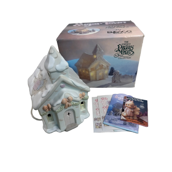 Enesco Precious Moments Sugar Town Lighted Chapel Figurine With Box Vintage 1992. A small decorative Christmas cottage figurine in a snowy white and pale blue finish, shown with its branded retail box and a few printed cards on a textured white surface.