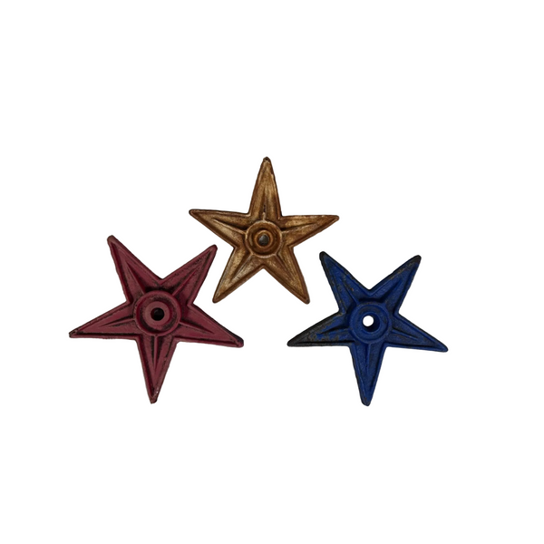 Set Of 3 Distressed Cast Iron Stars In Red White and Blue Finish Rustic Patina. Three decorative star-shaped wall hangings in red, gold, and blue, arranged on a textured white fabric background.