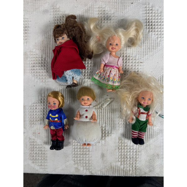 Lot of 5 Vintage 1990s Kelly and Friends Dolls Collectible Figures and Ornaments. Five vintage collectible dolls with long blonde and brown hair are arranged on a textured white fabric background. The dolls are dressed in various colorful outfits, including a red cape, a pink dress, a blue superhero costume, a white dress, and a green holiday outfit.