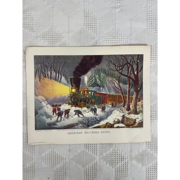 American Railroad Scene Lithograph by Currier and Ives Donald Art Co Vintage. A vintage printed illustration or postcard showing a steam locomotive traveling through snow at night, with workers and trees around it. The print is placed on a white textured fabric background.