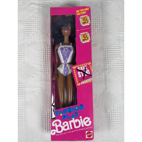 Vintage Mattel Fashion Play Barbie doll in its original pink packaging, featuring a doll with dark curly hair and a purple-and-white outfit, photographed on a textured white surface.