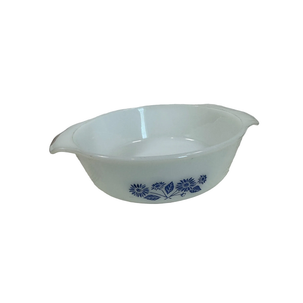 Anchor Hocking Fire King 1 Quart White Casserole Dish Blue Cornflower Design. A white oval casserole dish with blue floral patterns and side handles, resting on a textured white tablecloth against a plain wall.
