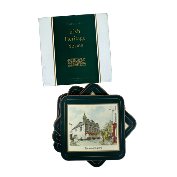 Pimpernel Irish Heritage Series Coasters Set Of 6 w Box Heat Resistant Vintage. A boxed set of square coasters displayed on a white textured fabric background. The top box reads 'Pembrook Irish Heritage Series,' and the coasters below feature dark green borders and printed scenic illustrations, including a building scene labeled 'Knole Co.