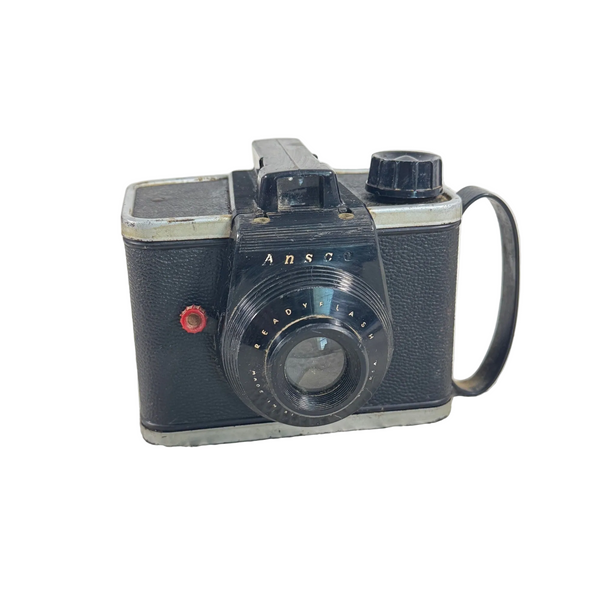 Vintage Ansco Readyflash 620 Film Camera Black 1950s Collectible Photography. A vintage ANSK camera with a black textured body, silver metal trim, and a black lens, resting on a textured white surface.