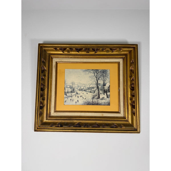 Vintage Gold Framed Winter Landscape With Skaters By Pieter Bruegel The Elder. A framed winter landscape print with a gold ornate frame and a yellow mat, hanging on a plain white wall.
