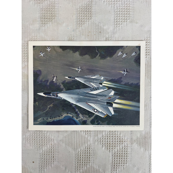 United States Air Force F111A Tactical Fighter Art Print Vintage 1960s Militaria. A vintage military art print depicting fighter jets flying over a landscape, mounted on a textured off-white quilted fabric background.
