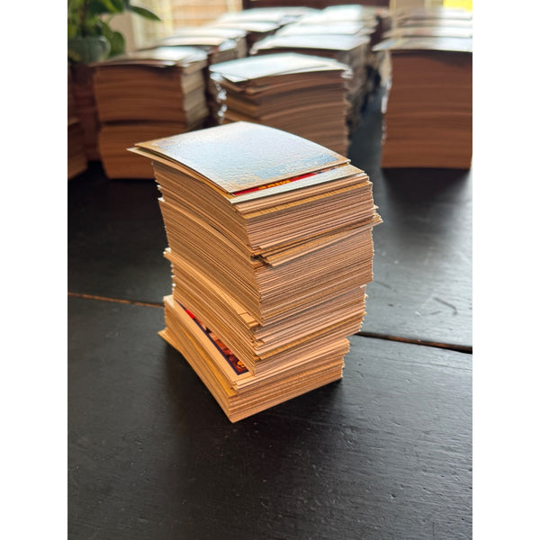 Bulk Lot Of 1 Pound Of 1980s Topps Baseball Trading Cards Assorted Teams Players. A stack of small rectangular cards or envelopes made from tan paper, standing on a dark tabletop, with more stacks blurred in the background.
