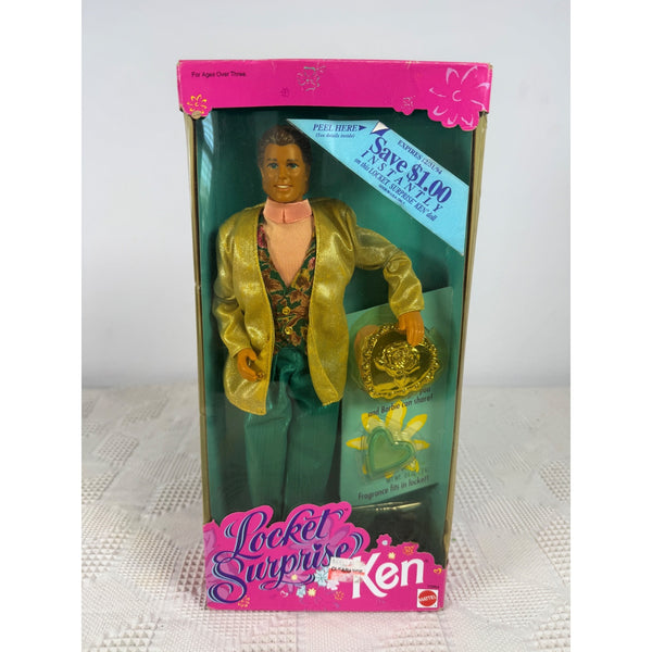 A boxed Ken doll labeled 'Locket Surprise!' with a gold jacket, green pants, and a hat inside the packaging, photographed against a light neutral background. Barbie Locket Surprise Ken Doll 1993 Mattel Vintage 10964 NIB