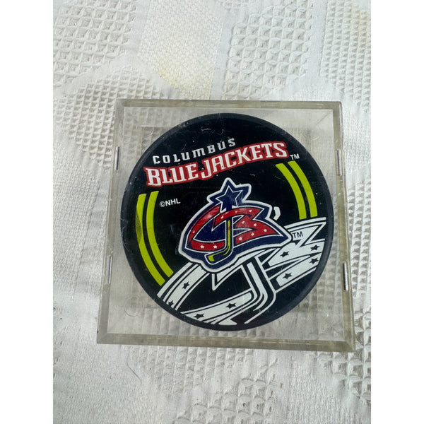 Columbus Blue Jackets Official NHL Licensed Hockey Puck Displayed In Case . A Columbus Blue Jackets NHL hockey puck displayed inside a clear plastic protective case, set against a textured white paper towel background.