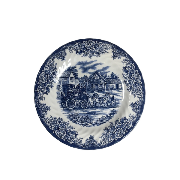 Royal Stafford Blue & White Fine Earthenware Plate w Coach Scene Made In England. A round white ceramic plate with a classic blue transfer design, featuring a central scene of a horse-drawn carriage and a floral border, displayed on a textured white quilted blanket.