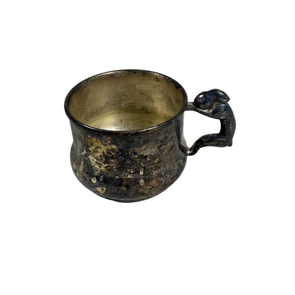 Vintage Sheridan Silver Co Baby Cup w Bunny Handle Silver On Copper Childrens. An antique tarnished pewter mug with a sculpted rabbit handle, resting on a textured white fabric surface.