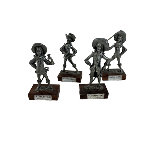 Les Étains Du Prince Handcrafted Pewter Musketeer Figurines Set Of 4 Wood Bases. Four small metallic figurines on dark wooden bases, arranged on a white textured fabric surface against a plain light background.