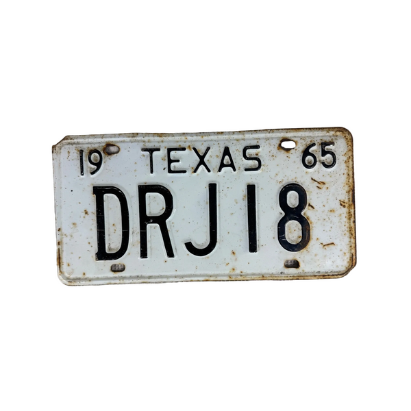 1965 Texas License Plate DRJ18 Vintage Metal White w Black Embossed Lettering. A vintage 1965 Texas license plate with the registration DRJ18, featuring a white background with black lettering and visible rust and wear, displayed on a textured light gray fabric background.