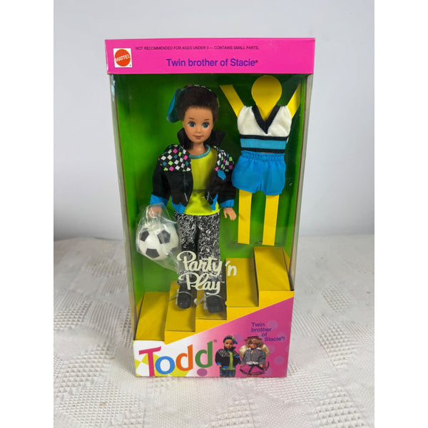 Vintage Mattel 'Todd' Party 'n' Play doll set in its original pink and green retail packaging, featuring a girl doll in a black jacket and patterned pants holding a soccer ball, with a blue and white athletic outfit displayed on a yellow stand inside. Party N Play Todd Doll Twin Brother Of Stacie 1992 Vintage Mattel 7903 NIB
