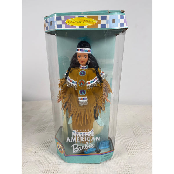 A boxed collectible Native American Barbie doll standing in a clear plastic display box with a teal and white patterned top band. The doll wears a tan fringed outfit with white, blue, and red beadwork, and the packaging text reads 'Fifth Edition Native American Barbie' and 'Collector Edition. Native American Barbie Doll Collectors Dolls Of The World Mattel 18558 NIB