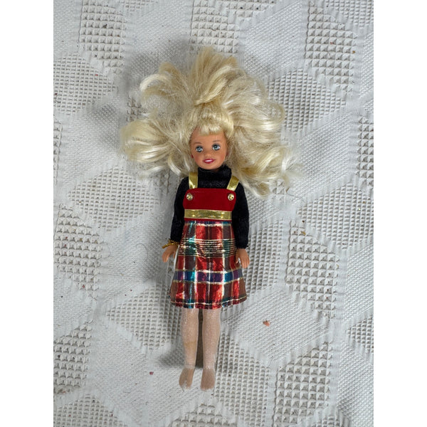 Vintage 1998 Stacie Sister of Barbie Doll Holiday Sister Plaid Dress Christmas. A vintage-style doll with blonde hair, wearing a black top and a red plaid pinafore dress, lying on a textured white fabric background.