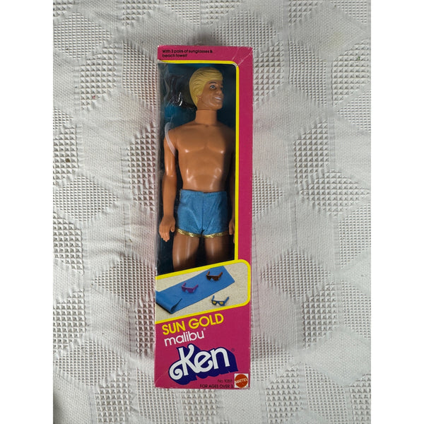 Vintage Ken doll in its original pink packaging, displayed on a textured white fabric background. The box features 'Sun Gold Malibu Ken' branding and shows the doll with blond hair and blue swim trunks. Sun Gold Malibu Ken Doll By Mattel Vintage 1983 with Sunglasses 1088 NIB