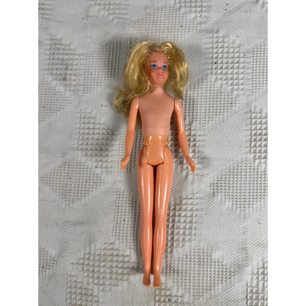 Vintage 1975 Growing Up Skipper Doll Little Sister Of Barbie Grows With Arm Turn. A vintage blonde doll with a peach-colored plastic body and hair, lying on a textured white fabric background.