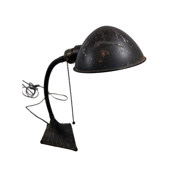 Vintage Art Deco Gooseneck Desk Lamp w Fluted Base and Metal Shade. A vintage dark metal desk lamp with a curved arm, dome-shaped shade, and pull-chain switch, resting on a white patterned surface against a light gray wall.