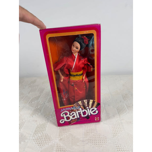 A vintage Japanese Barbie doll in its original pink packaging, held by a hand against a light gray background. Japanese Barbie Dolls Of The World Collection Red Kimono 1984 Mattel 9481 NIB 
