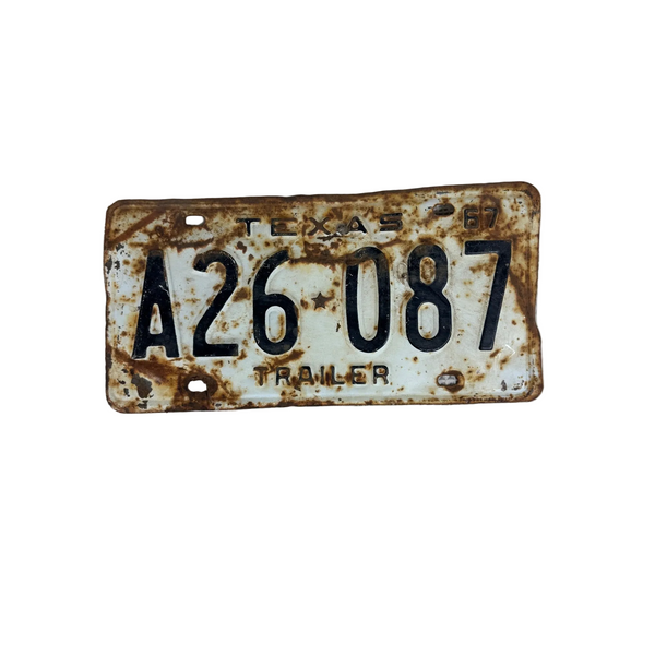 Vintage 1967 Texas Trailer License Plate A26 087 White Black Embossed Lettering. A vintage, heavily rusted Texas trailer license plate reading 'A26 087' on a textured white fabric background.