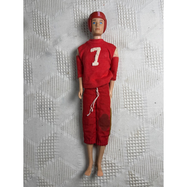 Original Ken MCMLX Football Outfit Doll Vintage Mattel Japan 1960s Red No 7. A vintage plastic doll with a red football uniform, number 7 on the chest, and a matching red helmet, standing against a textured white background.
