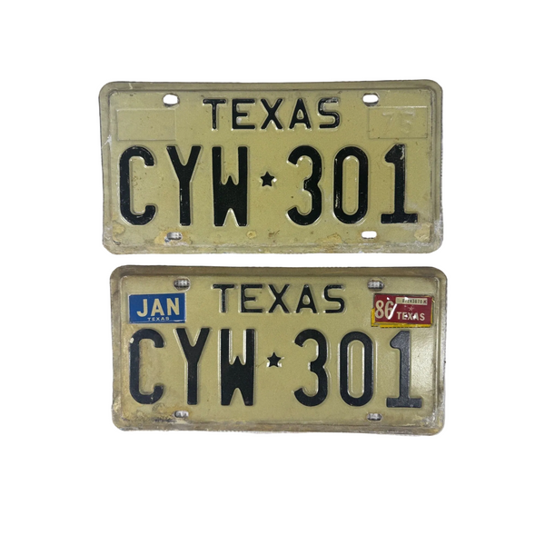 Pair Of Vintage Texas License Plates CYW 301 1975 White w Black Embossed Letters. Two vintage Texas license plates reading CYW 301, one in natural cream and one in yellowed beige, displayed on a textured white surface.