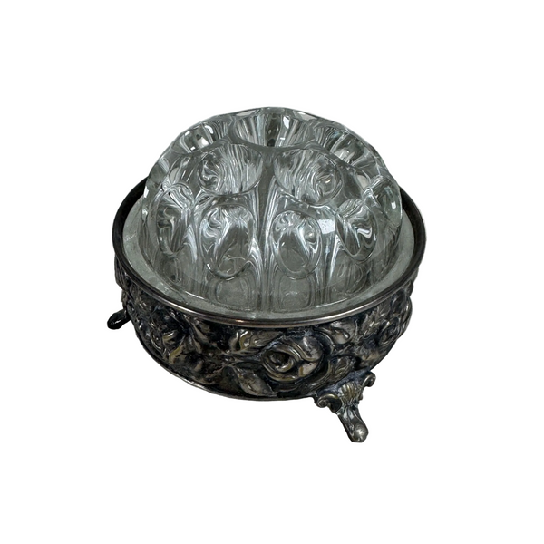 Vintage Silver Plated Floral Frog With Glass Top By De Uberti Italy c1950s. A vintage silver-tone footed bowl with an embossed floral pattern, holding a clear glass dome lid with a ribbed, textured pattern, set on a white textured fabric background.