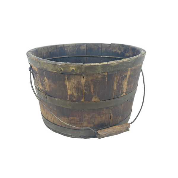 In good condition for the age. . A vintage wooden barrel-style bucket with dark brown stained wood, brass metal bands, and a wire handle, sitting on a white textured surface against a light blue background.