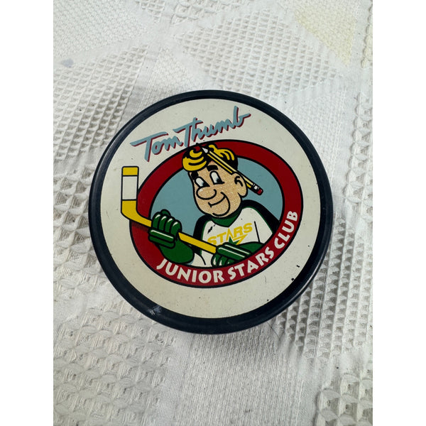 Dallas Stars Tom Thumb Junior Stars Club NHL Hockey Puck Made In Slovakia Vegum. A vintage circular hockey puck featuring the Tom Thumb Junior Stars Club logo, resting on a white textured fabric background.