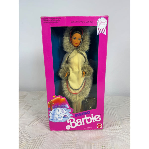 A boxed Barbie doll featuring an Eskimo-style outfit with a fur-trimmed hood and light dress, displayed in a bright pink Barbie box on a light surface against a pale wall. Eskimo Barbie Dolls Of The World Collection 1990 Special Edition 9844 NIB 
