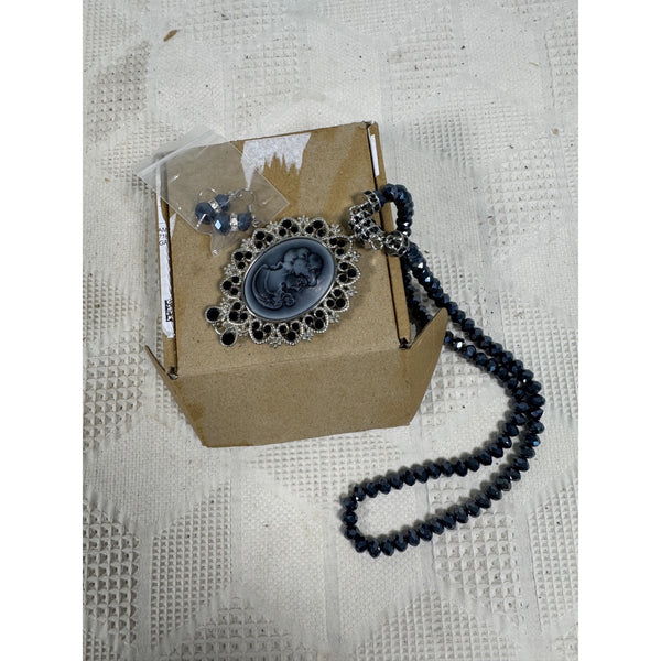 Cameo Necklace Black Beads Convertible Pendant Brooch and Matching Earrings Set. A dark blue beaded necklace with a silver filigree cameo pendant, shown next to its brown cardboard box packaging on a textured white fabric background.