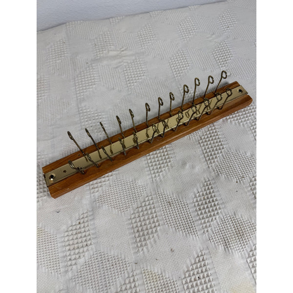 Vintage c1970s Wood and Brass Wall Mount Tie Rack or Belt Jewelry Hanger .A wooden wall-mounted rack with multiple curved metal hooks, photographed on a white textured fabric background.