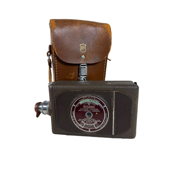 Vintage Bell and Howell Filmo Auto Load 8mm Movie Camera With Brown Leather Case. A vintage Brownie Manual Load film camera with a brown leather case, displayed on a textured white fabric surface against a neutral background.