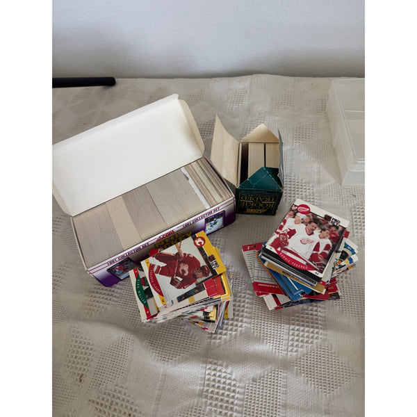 NHL Hockey Traded Cards Lot of Over 600 Cards 1990s Mixed Players and Teams. A collection of hockey trading cards and a card box arranged on a textured white tablecloth. Visible cards include a Santa Claus card and a Patrick Star card, with a box labeled '2004 WCHL PLAYOFFS'.