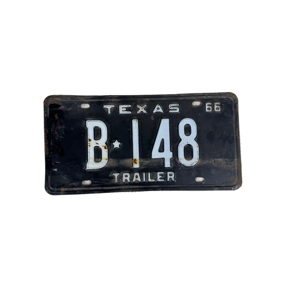 Vintage 1966 Texas Trailer License Plate B 148 Black w White Embossed Lettering. A vintage black Texas trailer license plate with white lettering and numbers, reading 'TEXAS B 148 TRAILER' and '66', placed on a textured off-white surface.