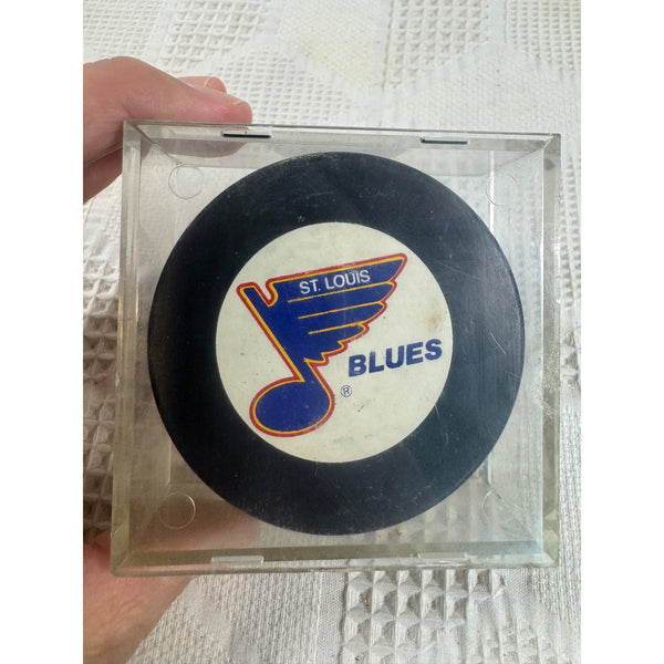 St Louis Blues Official NHL Licensed Hockey Puck Trench Mfg Slovakia Collectible. A St. Louis Blues hockey puck displayed inside a clear plastic case, held by a hand against a white textured background.